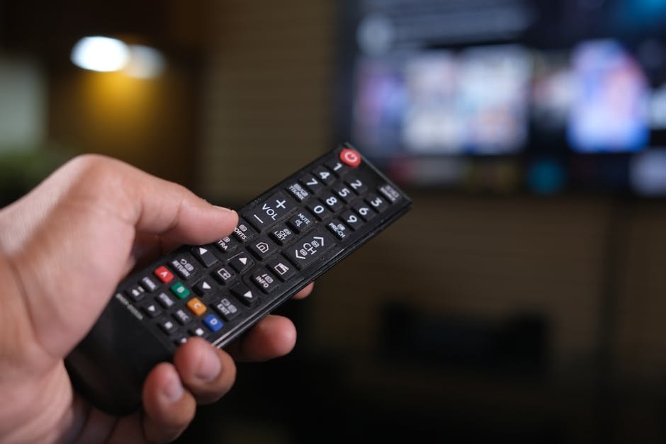A hand holding a TV remote control aimed at a television, illustrating the manual menu work needed to disable ACR